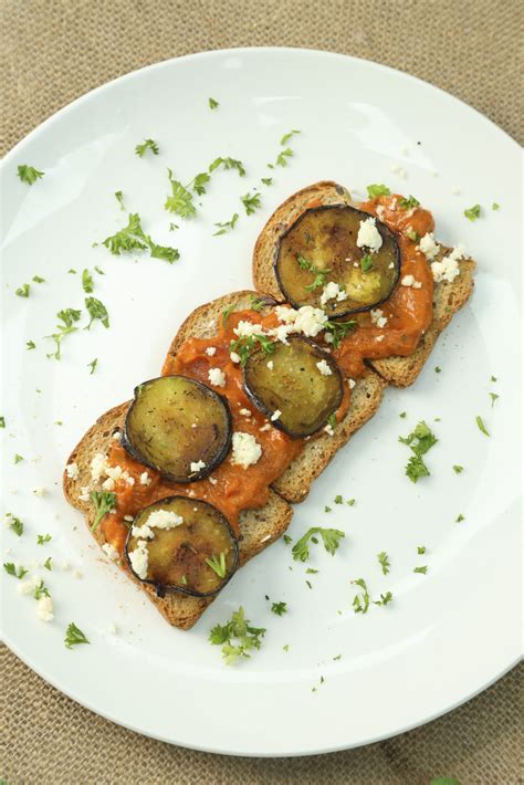 Plato de tostadas mediterráneas con pimientos asados y crema de berenjena decoradas con hierbas frescas