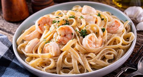 Plato terminado de fideos con crema de coco y camarones, decorado con semillas de ajonjolí y cebolla larga.