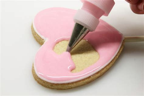 Primer plano de una mano delineando una galleta con glasa utilizando una manga pastelera y boquilla fina.