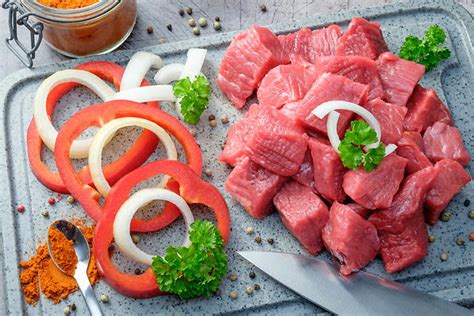 Ingredientes frescos para goulash incluyendo carne, cebollas, pimientos, y tomate