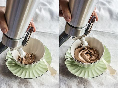 Foto de una espuma de chocolate servida artísticamente en un vaso, con un sifón al fondo.