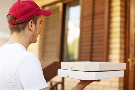 Fotografía de un repartidor de pizza entregando una caja de pizza a un cliente.