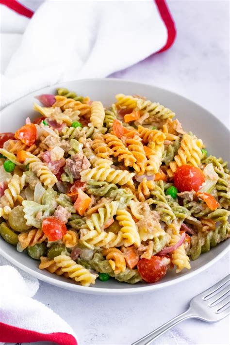Ensalada de pasta colorida con frutas, verduras y un aderezo cremoso servido aparte