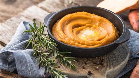 Fotografía gastronómica de un puré de camote decorado con una rodaja de mandarina fresca y tomillo sobre un plato artesanal.