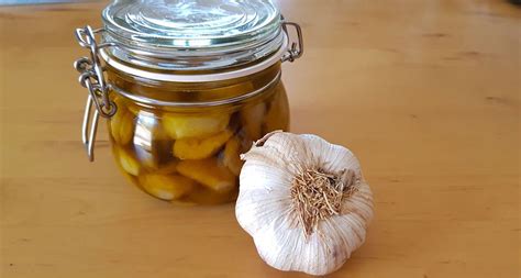 Un frasco de vidrio con ajos confitados y hierbas aromáticas en aceite de oliva, destacando su color dorado y la infusión de las especias.