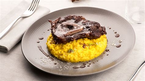 Plato de risotto alla milanese con su característico tono amarillo servido con una pieza de ossobuco al lado.