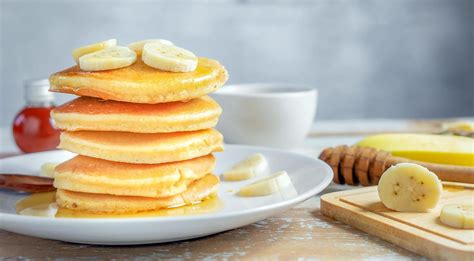 Fotografía de una pila de panqueques de banana decorados con rodajas frescas y miel.