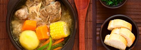 Ingredientes variados para la cazuela de cerdo: trozos de carne, verduras frescas como cebolla, zanahoria, patatas, pimiento, maíz, y condimentos.