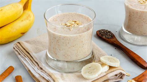 Vaso de licuado de frambuesa, avena y proteína, con frambuesas y avena esparcidas al lado