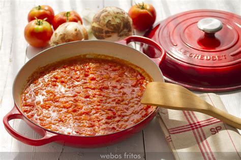 Cazuela plana con fritada de tomate y cebolla cocinándose a fuego medio.