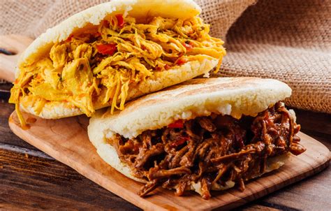 Fotografía detallada de arepas recién asadas con una textura dorada y crujiente sobre una superficie de madera.