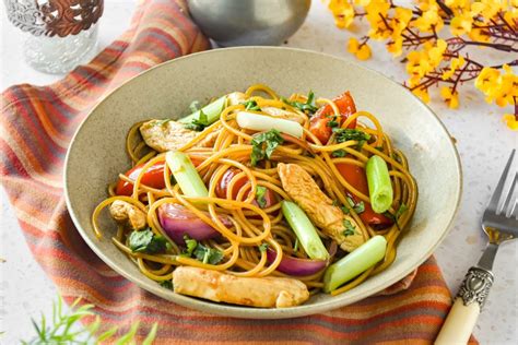 Fotografía gastronómica de un tallarín saltado recién servido con colores vibrantes de verduras y carne salteada.