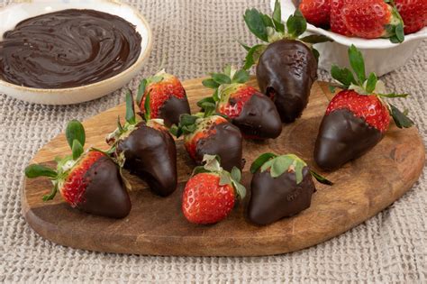Plato de fresas frescas bañadas en chocolate oscuro y blanco, con algunas espolvoreadas con frutos secos triturados
