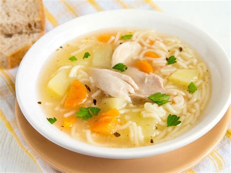 Fotografía de un tazón de sopa de pollo caliente con verduras frescas y fideos humeantes
