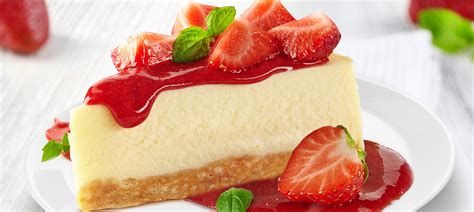 Fotografía de un cheesecake de fresa terminado, decorado con salsa de fresas y frutas frescas.