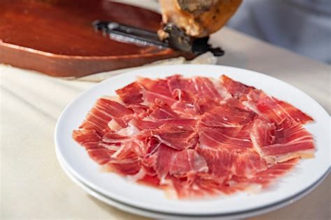 Foto de jamón casero cortado en finas rebanadas en un plato, con un sándwich de fondo
