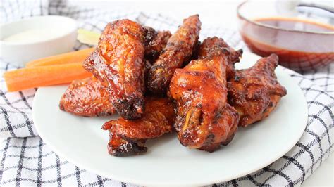 Plato de alitas de pollo glaseadas con salsa BBQ servidas en una bandeja con guarniciones variadas