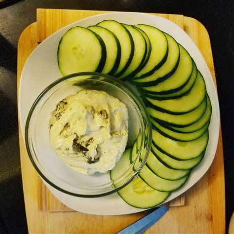 Fotografía de un hummus de jengibre decorado con láminas finas de pepino y un chorrito de aceite de oliva.