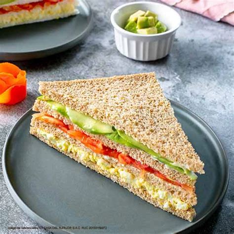 Fotografía de un sándwich triple terminado, mostrando las capas de palta, tomate y huevo