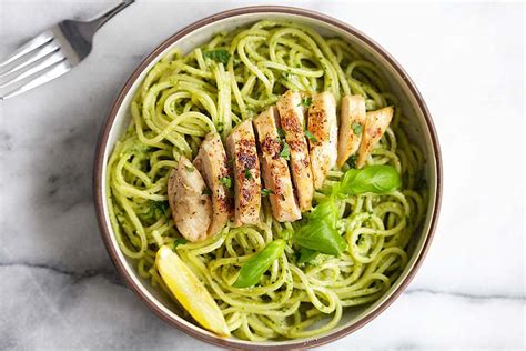 Plato servido de pasta con pollo dorado y salsa pesto verde vibrante, decorado con tomates cherry