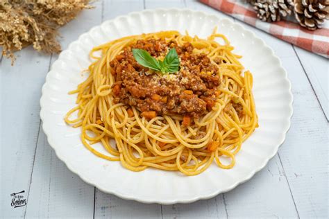 Plato de espaguetis a la boloñesa servido, decorado con albahaca fresca y queso parmesano.