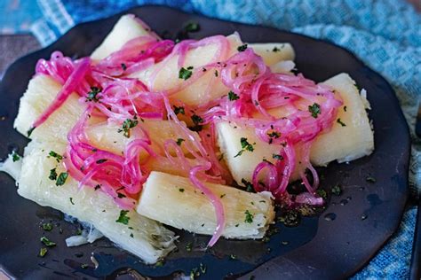 Imagen de una fuente de yuca hervida recién servida, bañada en una brillante salsa de mojo de ajo y decorada con perejil fresco o cebolla morada.