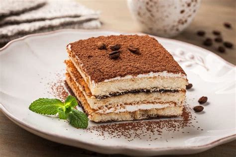 Foto detallada de un tiramisú en capas con cacao espolvoreado y vainillas visibles