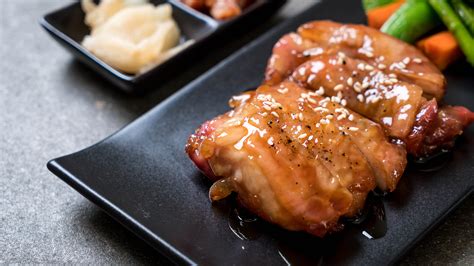 Primer plano de pechuga de pollo glaseada con salsa teriyaki brillante, decorada con semillas de sésamo y cebollino