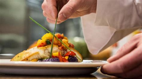 Chef concentrado emplatando un plato gourmet con pinzas