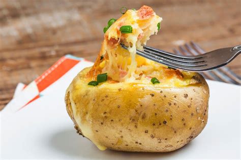 Imagen de una fuente de papas al horno con abundante queso cheddar fundido y verdeo por encima.