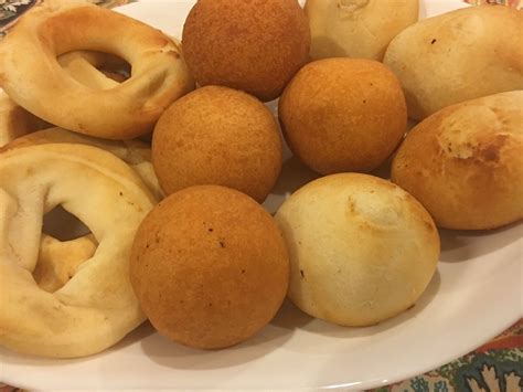 Fotografía de diversos pandebonos y almojábanas artesanales recién horneados sobre una bandeja de madera.