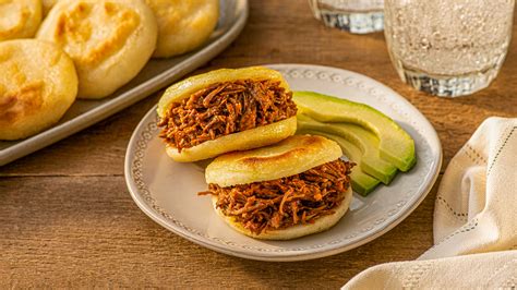 Plato de arepas abiertas y rellenas con pernil de cerdo, aguacate y queso, presentado en una mesa rústica.