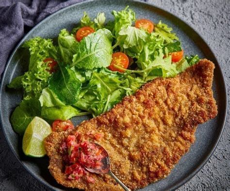 Imagen de una milanesa de res recién cocinada, dorada y crujiente sobre un plato elegante.