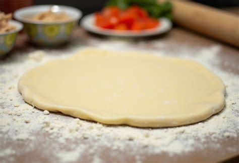 Fotografía de masa de empanada estirada sobre una superficie de trabajo junto a un cuenco con ingredientes secos.