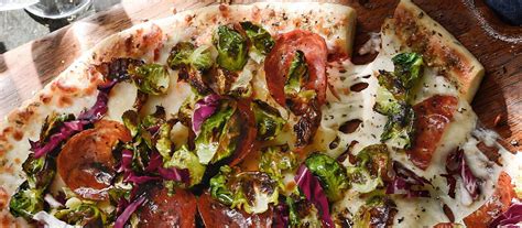 foto de una pizza recién horneada cubierta con una montaña de ensalada césar fresca y trozos de pollo dorado