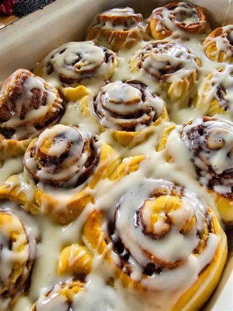 Cinnamon rolls recién horneados sobre una rejilla con glaseado cayendo