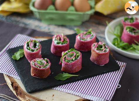 Plato elegante de rollitos de crepes rellenos de bresaola, queso crema y rúcula dispuestos en una bandeja.