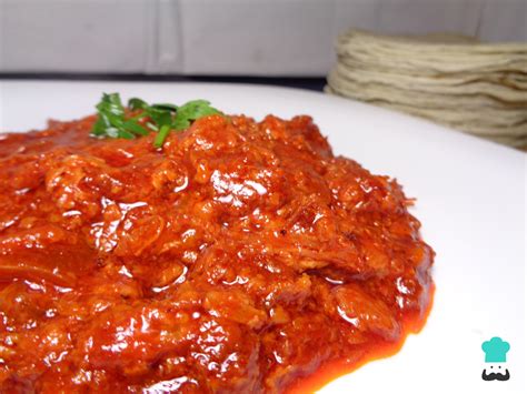 Chicharrón prensado cocinándose en una salsa rojiza.