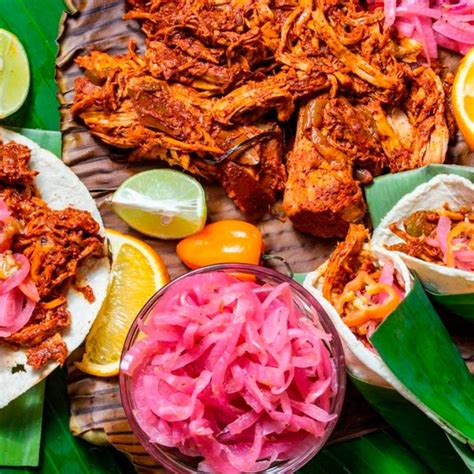 Cochinita pibil servida en una cazuela, con cebolla morada encurtida al lado.