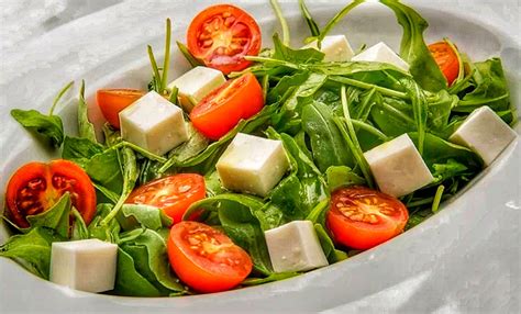 Imagen de una ensalada colorida con rúcula, tomate, aceitunas y escamas de queso, acompañada de crutones dorados.