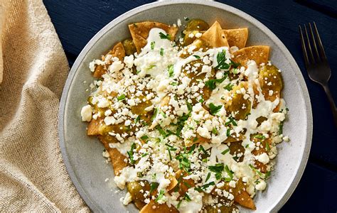 Plato de chilaquiles verdes decorados con salsa de molcajete, queso fresco y crema.