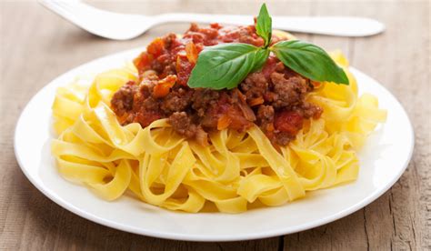 Un plato humeante de fideos caseros con salsa boloñesa y queso parmesano rallado.