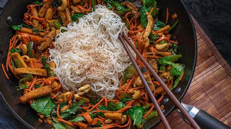 Foto detallada de un wok con fideos, vegetales crujientes y una salsa cremosa de cacahuetes