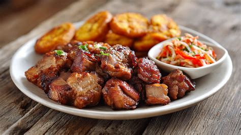 Fotografía detallada de un plato de Griot servido con plátanos fritos y una porción generosa de Pikliz