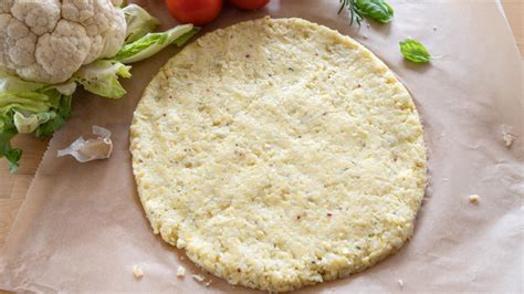 Imagen de la base de pizza de coliflor cruda extendida en una bandeja de horno.