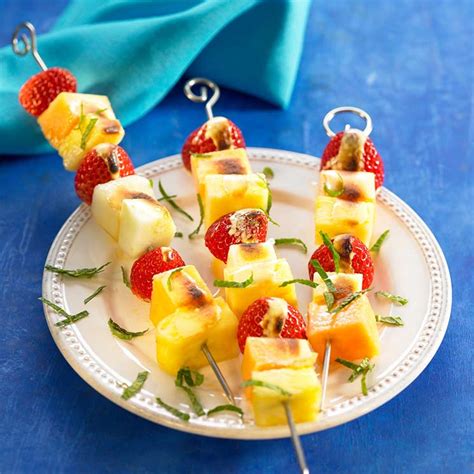 Brochetas con trozos de manzana, piña y fresas a la plancha, servidas con un cuenco de salsa de yogur.