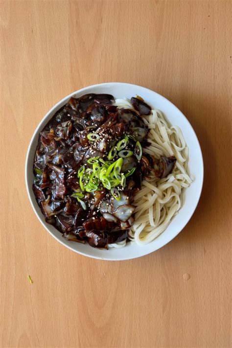 Plato de Jajangmyeon servido en un bol, con fideos cubiertos de salsa negra y decorado con cebollino y semillas de sésamo.