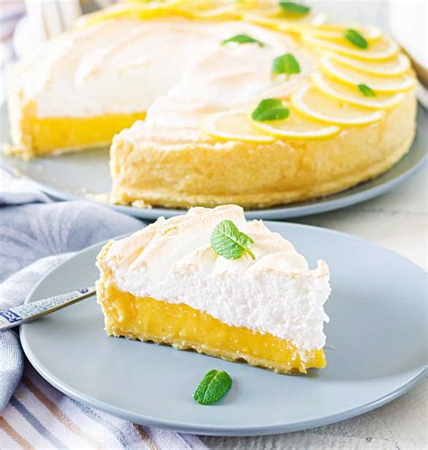 Foto artística de un pie de limón recién horneado con merengue dorado y rodajas de limón fresco