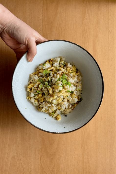Fotografía cenital de un bol de arroz salteado con huevo y brotes tiernos sobre una mesa de madera