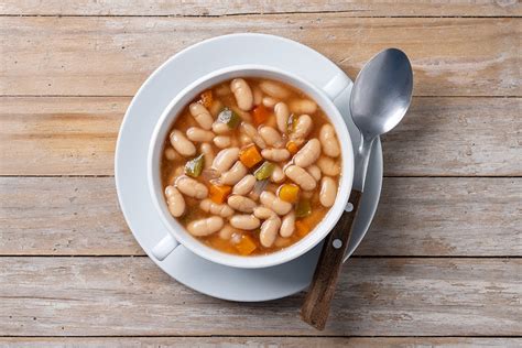 Fotografía apetitosa de un plato de frijoles blancos guisados con tomate, servido caliente.